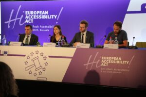 Four panelists sit at a table during the European Accessibility Act event in Brussels, July 2025. A purple banner with event details and a gavel graphic is displayed in front of them.