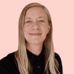 A staff member with straight, shoulder-length blonde hair and a black shirt smiles at the camera in front of a plain light pink background.