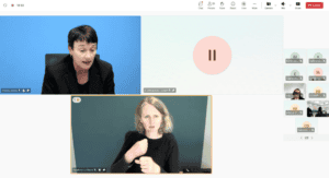 A woman speaks during a virtual meeting while a sign language interpreter translates in a separate video window. Other participant icons are visible on the right side.