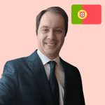 A man in a suit smiles at the camera with the Portugal flag displayed in the top right corner against a pink background.
