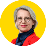 A member of the EUD Board with short grey hair, round glasses, and a red jacket over a dark scarf stands in front of a yellow background.