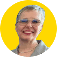 Person with short grey hair, glasses, and a grey collared shirt, smiling in front of a yellow background, representing the EUD Board.